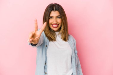 Pembe arka planda izole edilmiş genç Hintli kadın zafer işareti gösteriyor ve gülümsüyor..