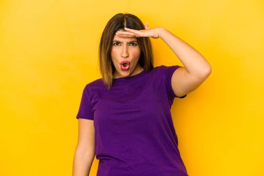 Sarı arka planda izole edilmiş genç Hintli kadın uzaklara bakıyor ve elini alnına koyuyor..