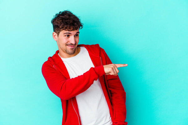 Молодой кавказский человек на голубом фоне смотрит в сторону улыбаясь, веселый и приятный.