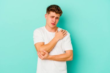 Kafkasyalı genç adam mavi arka planda izole edilmiş dirsek masajı yapıyor, kötü bir hareketin ardından acı çekiyor..