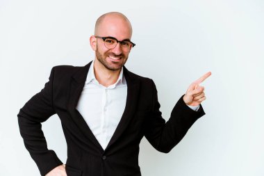 Genç, beyaz, kel bir adam mavi arka planda izole edilmiş. Gülümsüyor, işaret parmağıyla işaret ediyor..