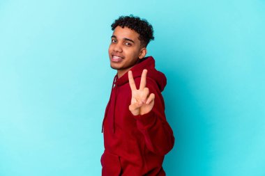 Genç Afro-Amerikan kıvırcık adamı mavi üzerine izole edilmiş zafer işareti gösteriyor ve gülümsüyor..