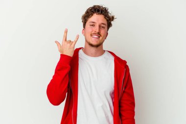 Beyaz arka planda izole edilmiş genç beyaz bir adam parmaklarıyla kaya hareketi gösteriyor.