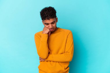 Genç Afro-Amerikalı kıvırcık adam mavi üzerine izole edilmiş üzgün ve dalgın hisseden, kopyalama alanına bakan.