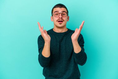 Kafkasyalı genç adam mavi arka planda izole edildi. Şaşırdı ve şok oldu..