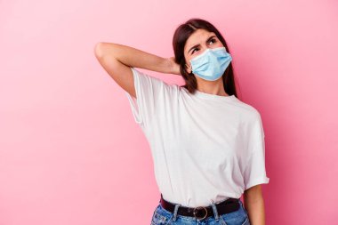 Virüs maskesi takan beyaz bir kadın pembe arka planda izole edilmiş kafasının arkasına dokunuyor, düşünüyor ve bir seçim yapıyor..