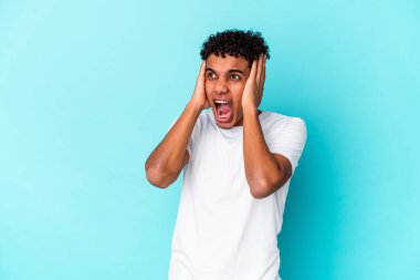 Genç Afro-Amerikalı kıvırcık adam, mavi kulaklarla izole edilmiş, elleri kulaklarda, çok fazla ses duymamaya çalışıyor..