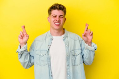 Sarı arka planda izole genç beyaz adam şans dilemek için şans diliyor.