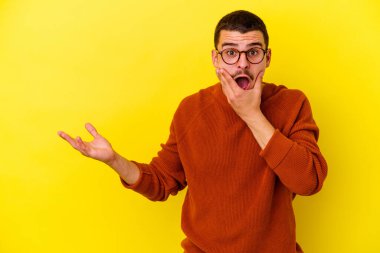 Sarı arka planda izole edilmiş beyaz bir genç, bir avuç içinde fotokopi alanı tutuyor, el üstünde tutuyor. Şaşırmış ve mutlu..