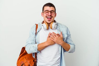 Beyaz arka planda müzik dinleyen beyaz tenli genç bir öğrenci ellerini kalbe ve mutluluk kavramına koyarak gülüyor..