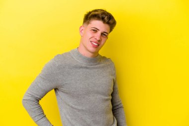 Sarı arka planda izole edilmiş genç beyaz adam ellerini kalçalarına koyuyor..