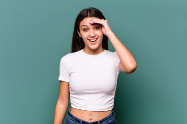 Mavi arka planda izole edilmiş genç Hintli kadın yüksek sesle bağırıyor, gözlerini açık ve ellerini gergin tutuyor..