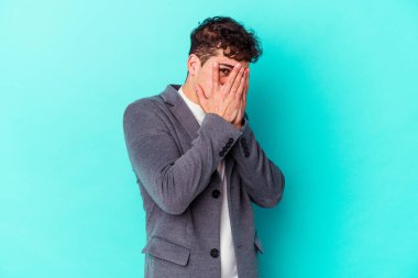 Kafkasyalı genç adam mavi arka planda izole edilmiş. Korkmuş ve gergin parmaklarıyla göz kırp..