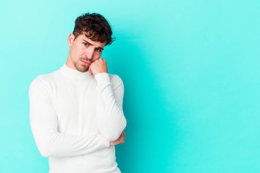 Mavi arka planda izole edilmiş, üzgün ve dalgın hisseden, kopyalama alanına bakan genç beyaz bir adam..