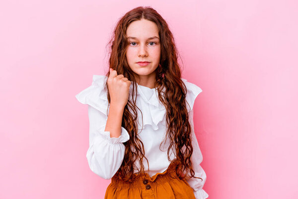 Маленькая белая девочка на розовом фоне показывает кулак к камере, агрессивное выражение лица.