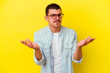 Kafkas asıllı genç adam sarı arka planda izole edilmiş şüphe içinde ve sorgulama sırasında omuz silkiyor..