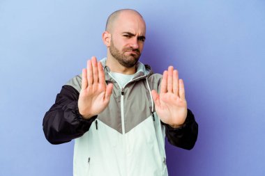 Kafkasyalı genç kel adam mor arka planda izole edilmiş elini uzatmış, dur işareti gösteriyor, bu da seni engelliyor..