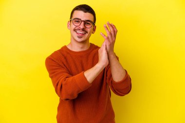 Sarı arka planda izole edilmiş genç beyaz adam enerjik ve rahat hissediyor, ellerini ovuşturuyor kendinden emin..