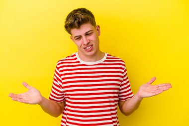 Sarı arka planda izole edilmiş genç beyaz bir adam elinde avuç içi bir şeyle kameraya sunuyor..