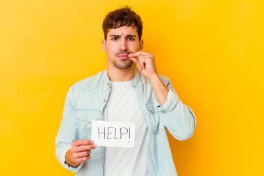 Genç, beyaz bir adam yardım levhası tutuyor. Parmakları dudaklarında ve bir sırrı saklıyor..