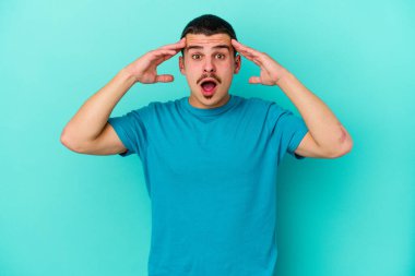 Mavi arka planda izole edilmiş genç beyaz adam yüzünün yarısını palmiye ile kaplayarak eğleniyor..