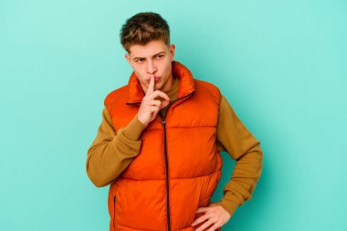 Mavi arka planda izole edilmiş genç beyaz bir adam ya sır saklıyor ya da sessizlik istiyor..