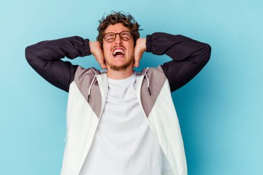 Mavi arka planda izole edilmiş gözlüklü genç beyaz adam öfkeyle bağırıyor..