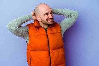 Kafkasyalı genç kel adam mor arka planda izole edilmiş. Kendine güveniyor, elleri başının arkasında..