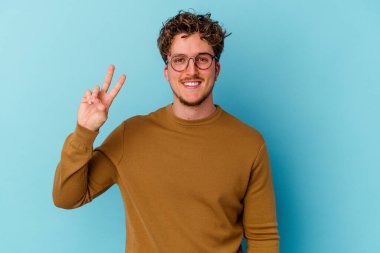 Mavi arka planda gözlüklü genç beyaz adam iki numarayı parmaklarıyla gösteriyor..