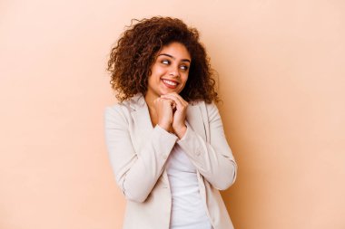 Bej arka planda izole edilmiş genç Afrikalı Amerikalı kadın ellerini çenesinin altında tutuyor ve mutlu bir şekilde yan tarafa bakıyor..