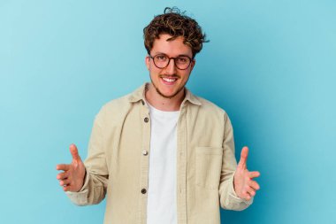 Mavi arka planda gözlüklü genç beyaz adam iki eliyle bir şey tutuyor, ürün sunumu..