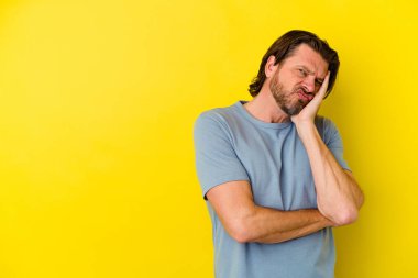Sarı arka planda izole edilmiş orta yaşlı beyaz bir adam üzgün ve dalgın bir şekilde fotokopi odasına bakıyor..