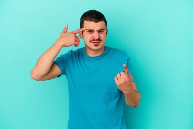 Mavi arka planda izole edilmiş genç beyaz adam işaret parmağıyla bir hayal kırıklığı jesti gösteriyor..