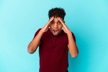 Genç Afro-Amerikalı kıvırcık adam mavi üzerine izole edilmiş. Yüzünün yarısını palmiye ile kaplayarak eğleniyor..