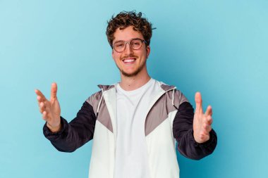 Mavi arka planda gözlüklü genç beyaz adam kameraya sarıldığı için kendinden emin..