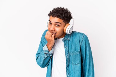 Genç Afro-Amerikalı kıvırcık adam kulaklıklı, tırnak yiyen, gergin ve endişeli bir şekilde müzik dinliyor..