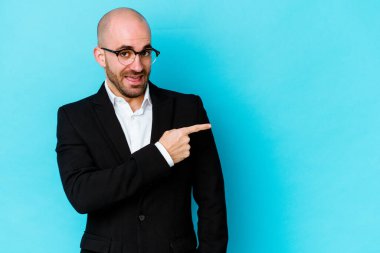 Kafkasyalı genç adam mavi arka planda izole edilmiş gülümsüyor ve boş alanda bir şeyler gösteriyor..