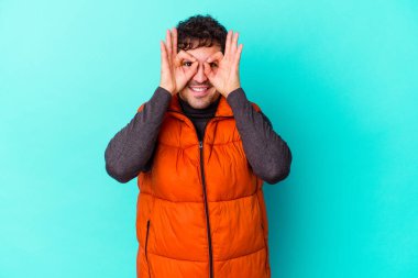 Mavi arka planda izole edilmiş genç beyaz adam gözlerinde sorun olmadığını gösteriyor.