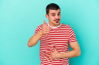 Mavi arka planda izole edilmiş genç beyaz adam karnına dokunuyor, nazikçe gülümsüyor, yemek yiyor ve tatmin oluyor..