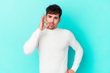 Genç beyaz adam mavi arka planda izole edilmiş ve parmakları dudaklarında bir sır saklıyor..