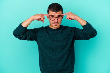 Kafkasyalı genç adam mavi arka planda izole edilmiş bir göreve odaklanmış, parmaklarını işaret ediyor..