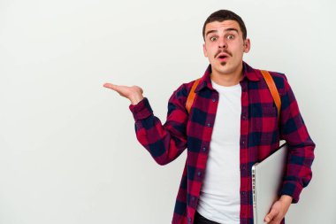 Beyaz arka planda izole edilmiş dizüstü bilgisayar tutan beyaz tenli genç bir öğrenci avuç içi fotokopi alanını tutmaktan etkilenmiş..