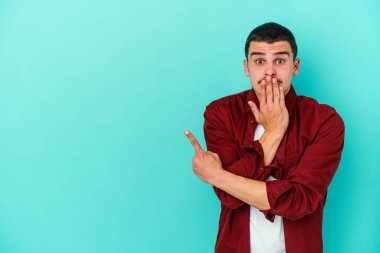 Mavi arka planda izole edilmiş genç beyaz adam yan tarafı işaret ediyor.