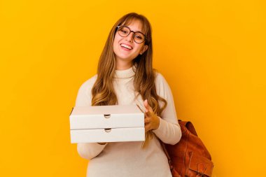 İzole edilmiş arka planda pizza tutan genç beyaz kadın mutlu, güler yüzlü ve neşeli..