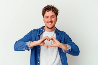 Beyaz arka planda izole edilmiş genç beyaz bir adam gülümsüyor ve elleriyle kalp şekli gösteriyor..