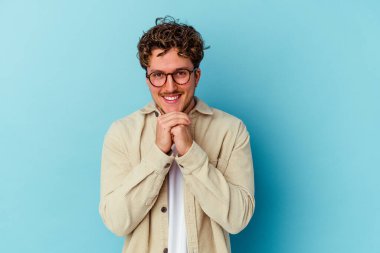 Mavi arka planda gözlük takan genç beyaz adam ellerini çenesinin altında tutuyor ve mutlu bir şekilde yan tarafa bakıyor..