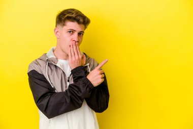 Sarı arka planda izole edilmiş genç beyaz adam yan tarafı işaret ediyor.