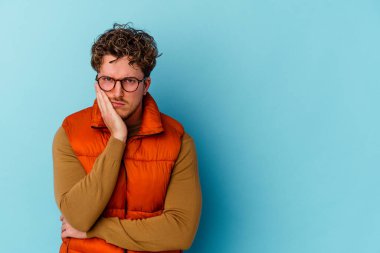 Mavi arka planda gözlüklü, üzgün ve dalgın hisseden, kopyalama alanına bakan beyaz bir adam..