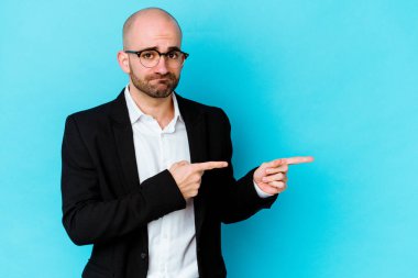 Genç beyaz tenli kel adam mavi arka planda izole edildi. İşaret parmağıyla fotokopi alanını işaret ederek şok oldu..