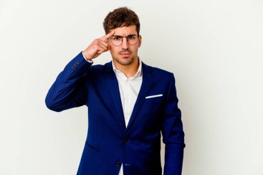 Beyaz arka planda izole edilmiş genç bir beyaz iş adamı şakağı işaret ediyor, düşünüyor, bir göreve odaklanıyor..